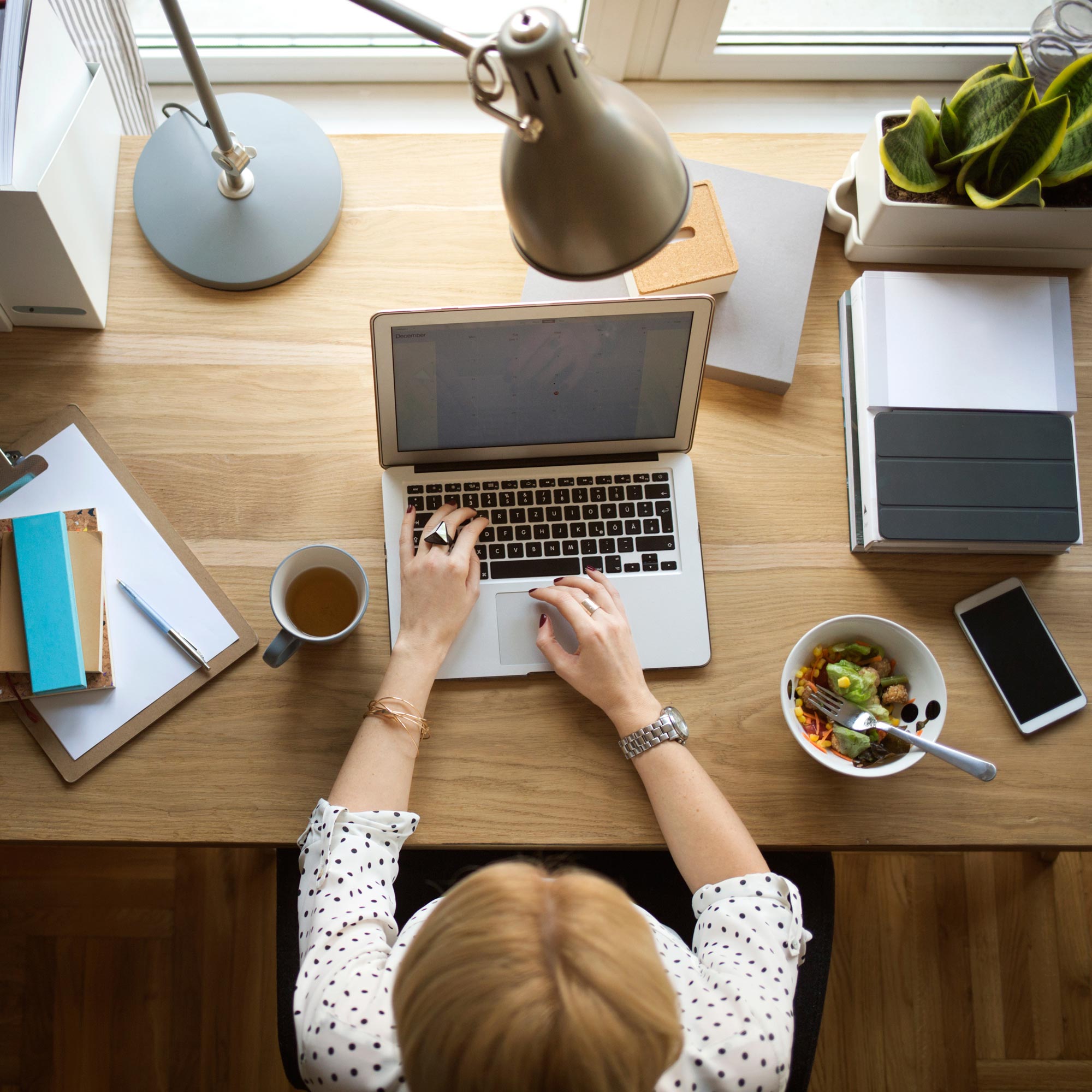 Kvinna sitter hemma på sitt kontor, jobbar på sin laptop och äter sallad
