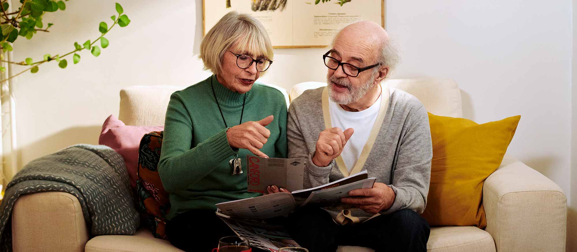 Äldre par sitter i soffan och tittar på en broschyr